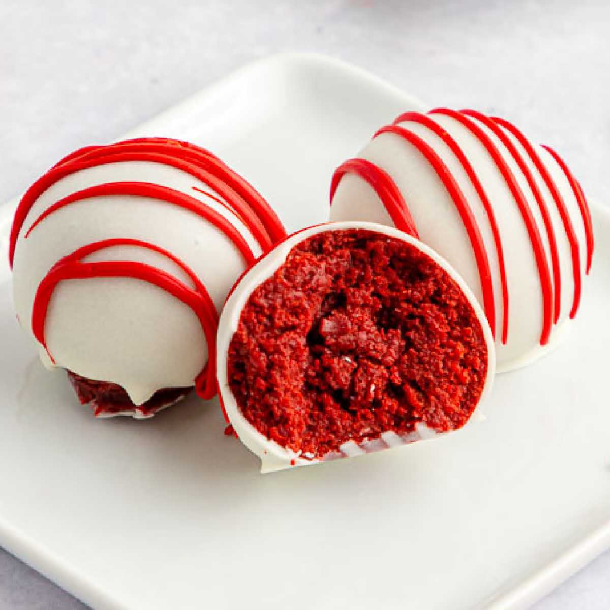 Close up of three Red Velvet Cake Balls on a white plate with a bite taken out of one.