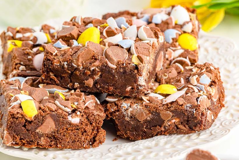 Front close up of squares of brownies with Cadbury Mini Eggs stacked on a plate.