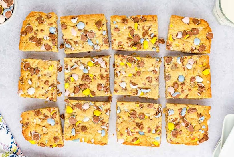 Overhead view of Cadbury tray bake bars cut into squares on parchment paper.