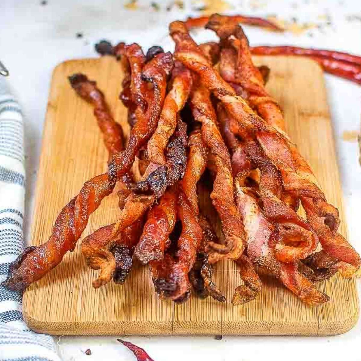 Air fryer twisted bacon piled on a wooden cutting board.