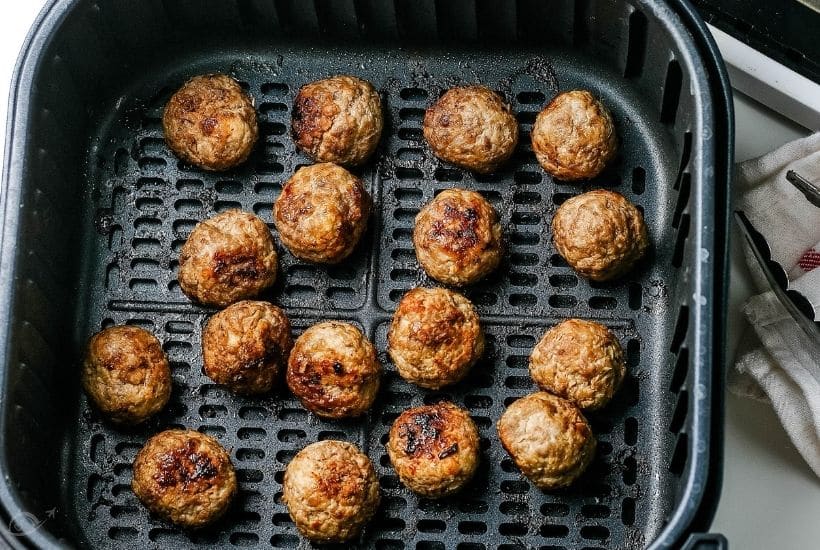 Cooked meatballs in an air fryer basket.