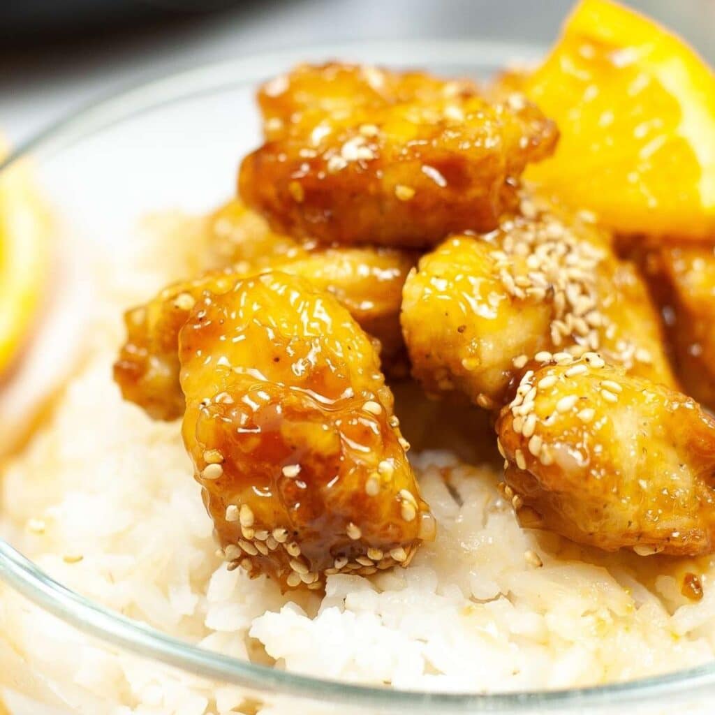 Closeup view of clear bowl filled with white rice and air fryer orange chicken garnished with sesame seeds.