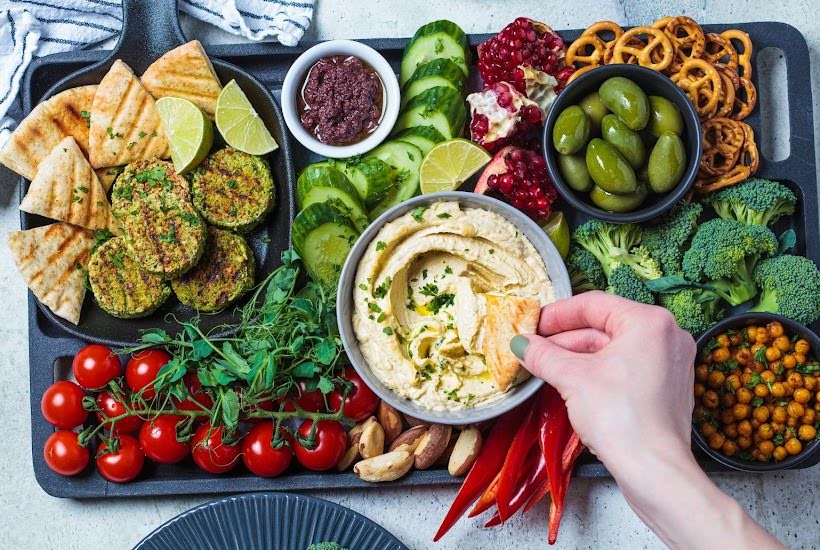 A platter filled with sliced vegetables, pretzels, fruits, dips and other cheap snack food ideas.