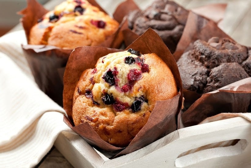A towel lined tray filled with a variety of muffins.