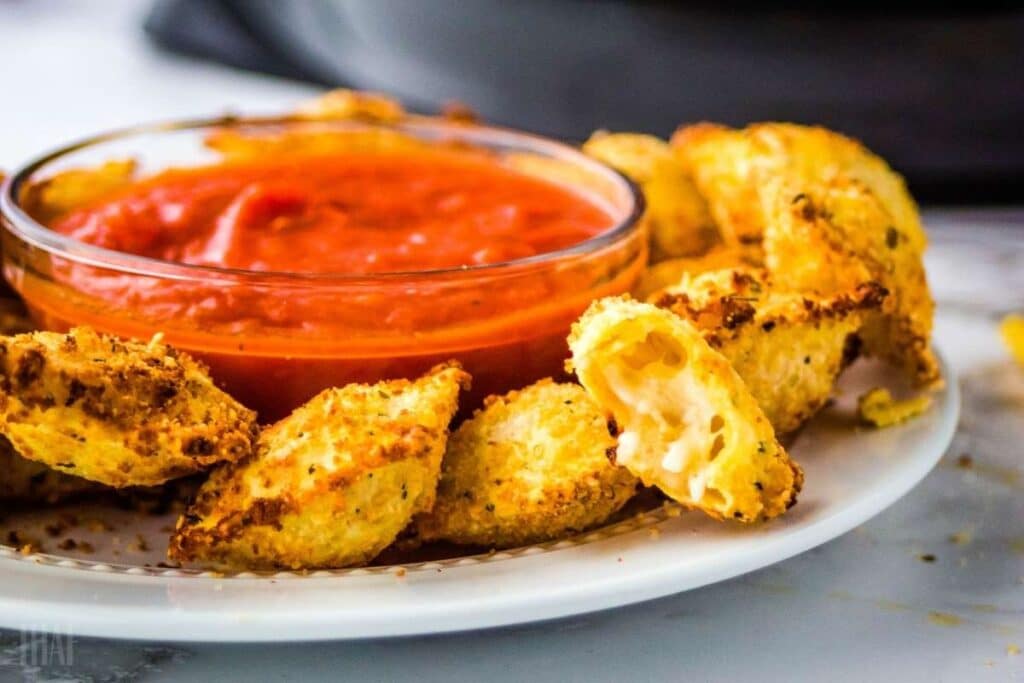 Air fried ravioli with a bowl of marinara sauce on a white plate.