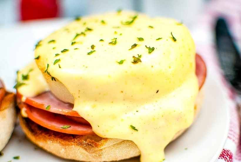 Closeup view of air fried eggs Benedict garnished with chopped parsley and covered in hollandaise sauce.