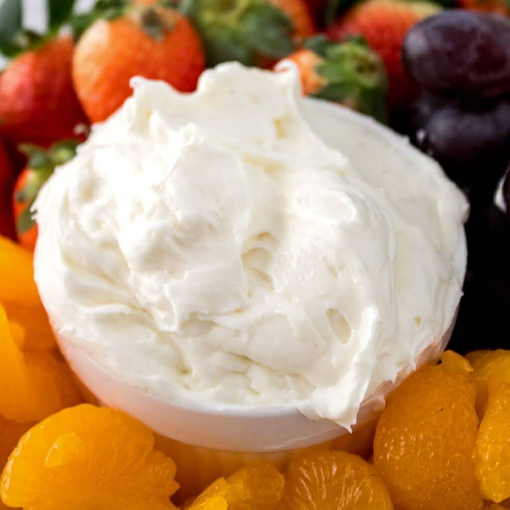 Closeup view of white bowl filled with homemade fruit dip surround by mandarin oranges, grapes and strawberries.
