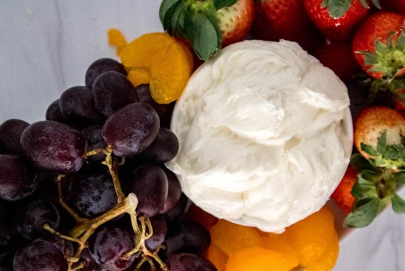 Top view of bowl of homemade fruit dip with grapes, oranges and strawberries.