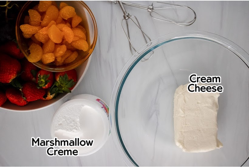 Ingredients to make marshmallow fluff fruit dip with a bowl of mixed fruits.