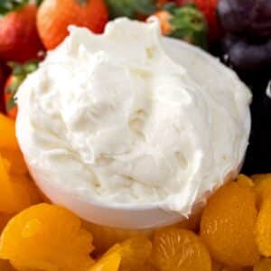 Closeup view of fruit dip with marshmallow fluff and cream cheese surrounded by oranges and other fruits in the background.