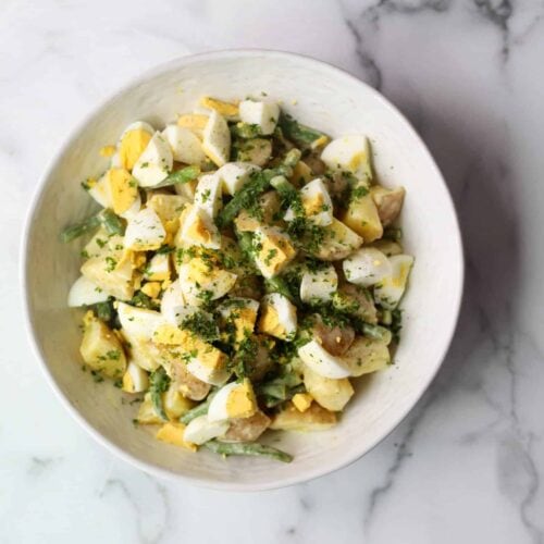 Potato salad with green beans and chopped boiled eggs in a white serving bowl.