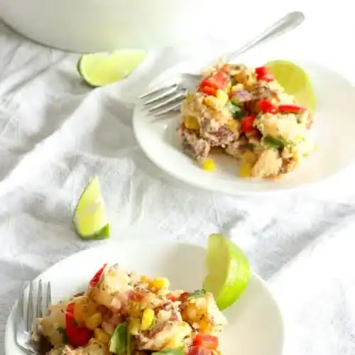 Two servings of Southwest potato salad garnished with lime wedges on white plates with the serving bowl in the background.