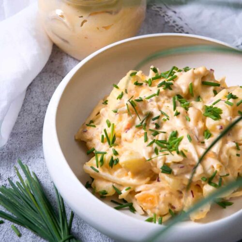 Creamy potato salad made with kimchi in a white serving bowl and garnished with chopped chives.