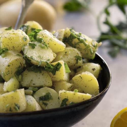 Potato salad with oil and herbs in a black bowl.