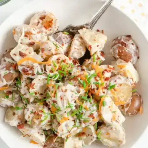 Potato salad loaded with bacon, cheese and chopped chives in a white serving bowl.