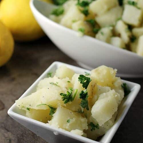 A simple herb and oil dressed Arabic potato salad in a square bowl.