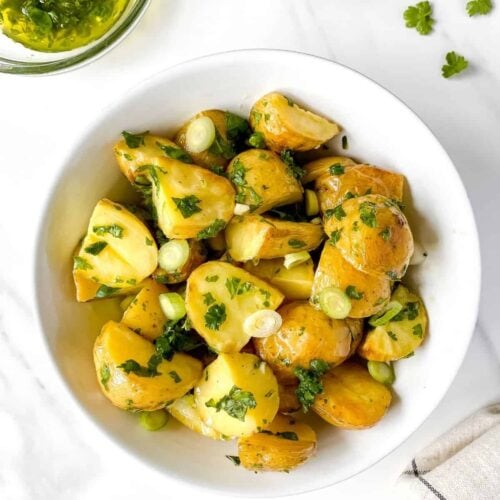 A simple roasted potato salad with sliced green onions and an herb dressing in a white serving bowl.