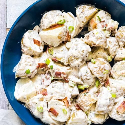 Loaded ranch potato salad with creamy sauce in a blue serving bowl.