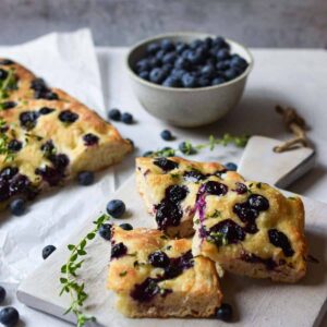 Slices of blueberry thyme focaccia bread on a wooden cutting board.