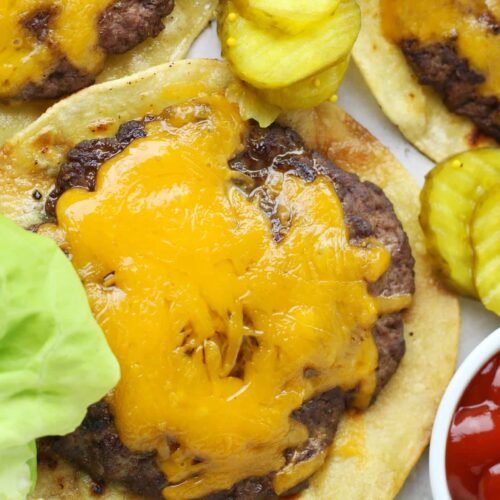 Smashed burger with melted cheese on a tortilla wrap surrounded by pickles, lettuce and ketchup.