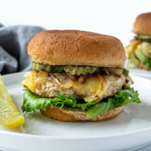 Turkey smash burger with cheese, onions, pickles and lettuce on a white plate.