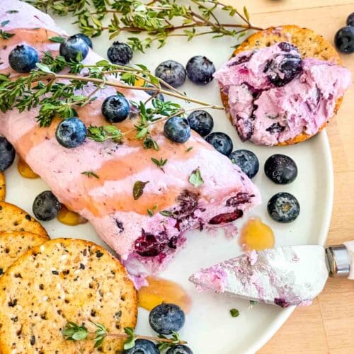 A log of blueberry goat cheese spread surrounded by fresh berries and crackers.