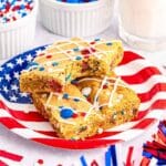 Two slices of M&M cookie bars, one with a bite removed, on a flag plate.