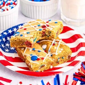 Two slices of M&M cookie bars, one with a bite removed, on a flag plate.