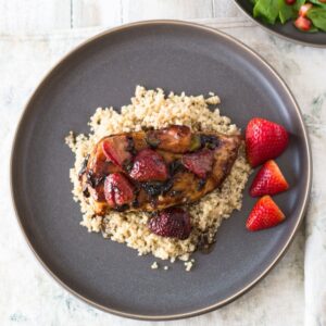Strawberry balsamic chicken with couscous and sliced strawberries on a gray plate.
