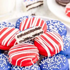 A plate of patriotic themed red, white and blue coated sandwich cookies with sprinkles and drizzle.