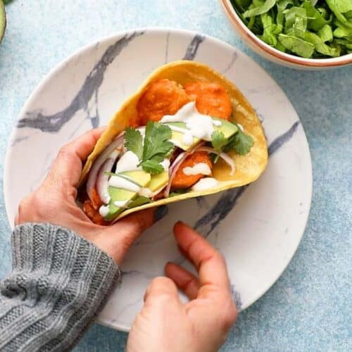 A hand holding a soft taco with buffalo shrimp.