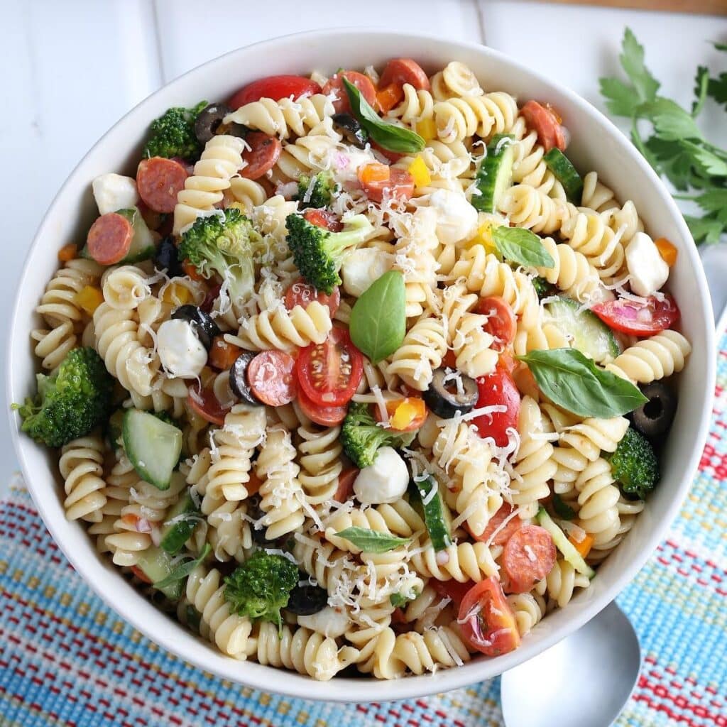 Top view of white bowl filled with rotini pasta salad garnished with shredded cheese and basil.