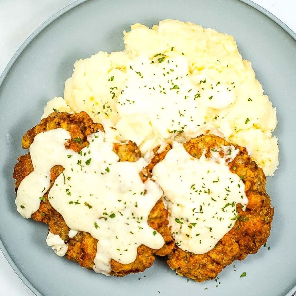 Overhead view of two fried steaks with gravy and mashed potatoes on a gray plate.