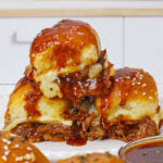 A stack of three beef brisket sliders with cheese and barbecue sauce on a white plate.