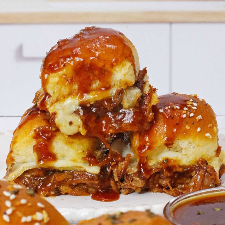A stack of three beef brisket sliders with cheese and barbecue sauce on a white plate.