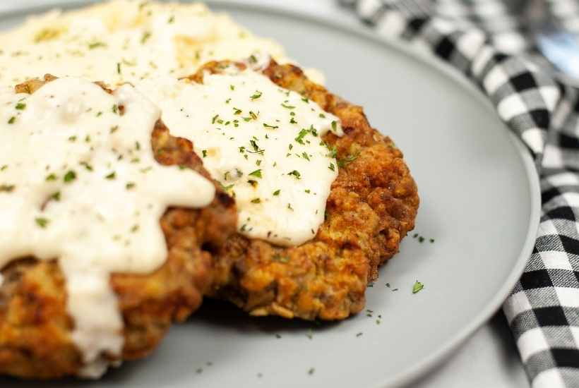 Front view of air fried chicken fried steak with gravy and mashed potatoes on a grey plate with text overlay.