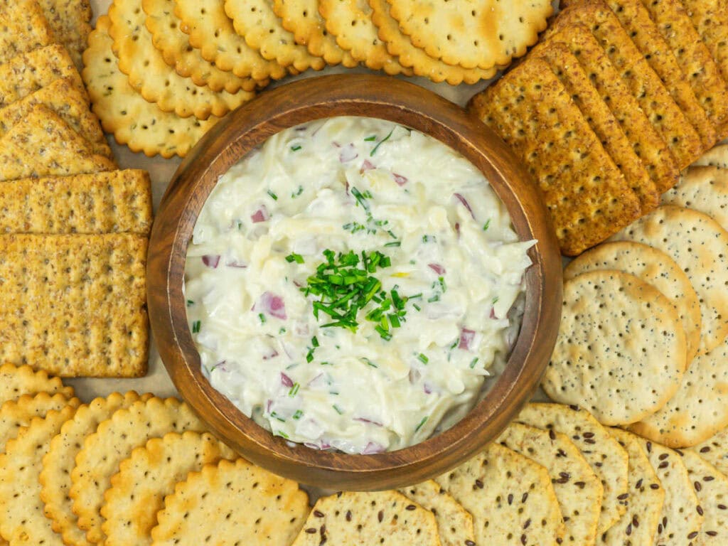 Top view of a wooden bowl filled with Kroger Jarlsberg cheese dip surrounded by crackers.