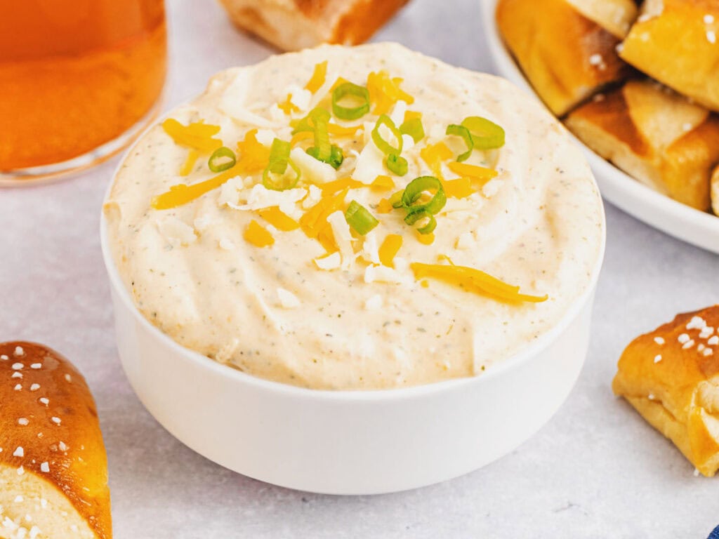 Closeup view of a bowl of beer cheese dip with ranch surrounded by soft pretzel pieces.