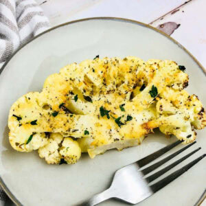 Roasted cauliflower steak on a white plate with a fork.