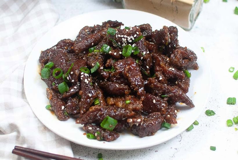 Crispy copycat PF Changs Mongolian beef garnished with green onion and sesame seeds on a white plate.