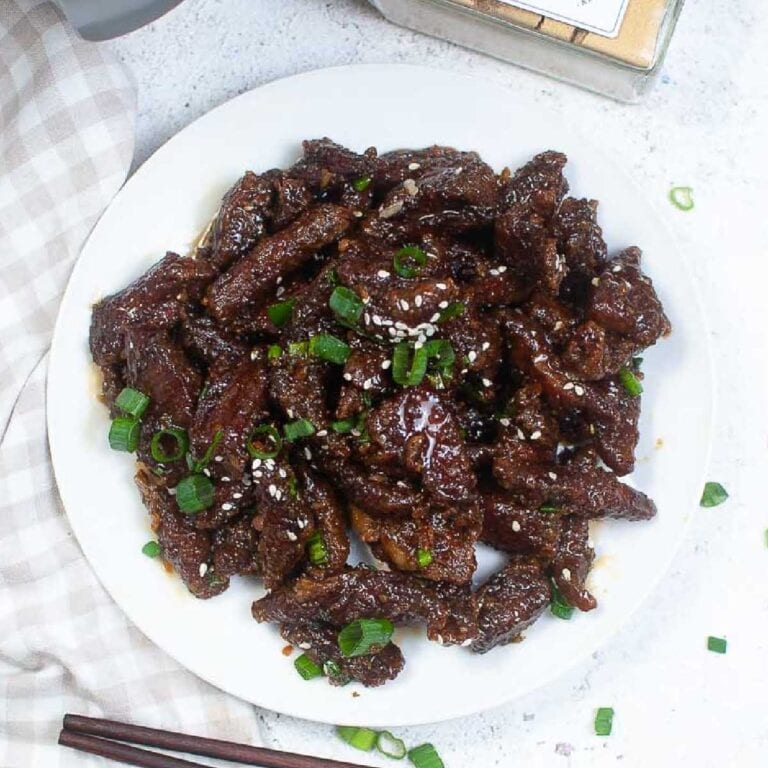 Top view of air fryer Mongolian beef on a white plate with sesame seeds and green onions.