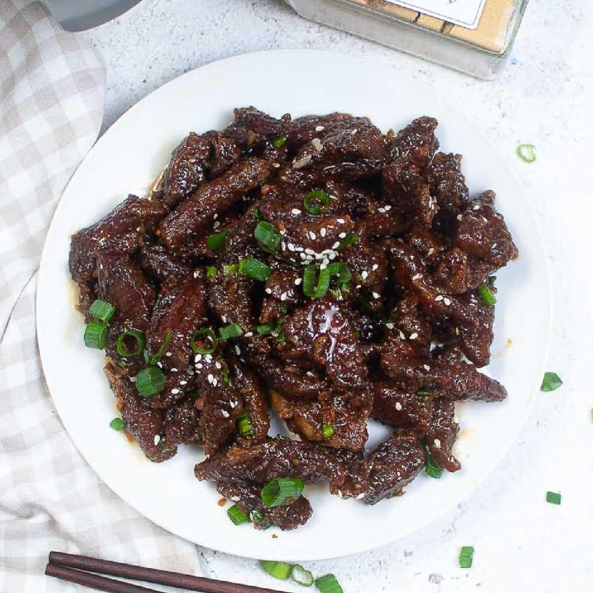 Top view of air fryer Mongolian beef on a white plate with sesame seeds and green onions.