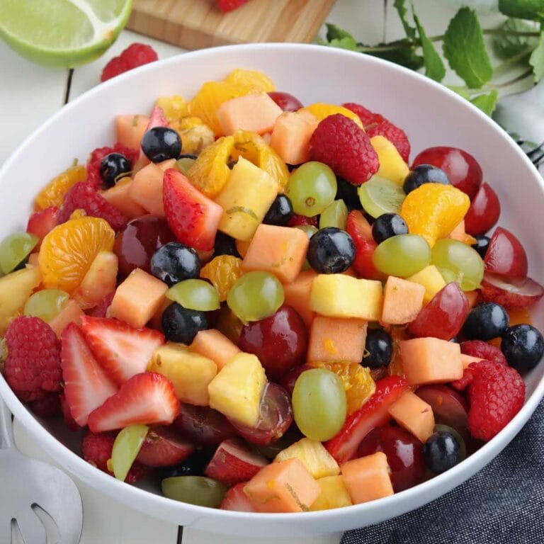 White bowl filled with fresh fruit salad with honey lime dressing.