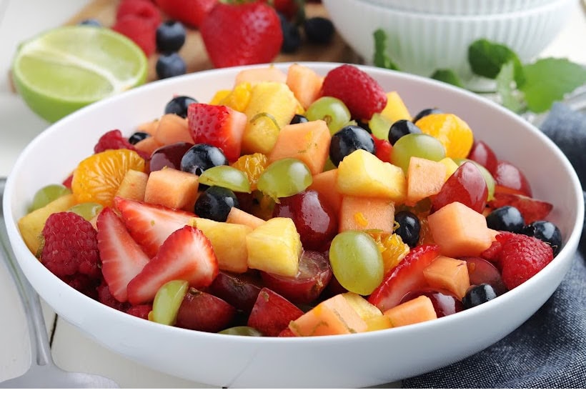 Side view of rainbow fruit salad with fruits and bowls in the background.