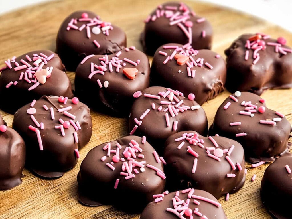 Copycat Reese's chocolate covered peanut butter hearts with pink sprinkles on a wooden cutting board.