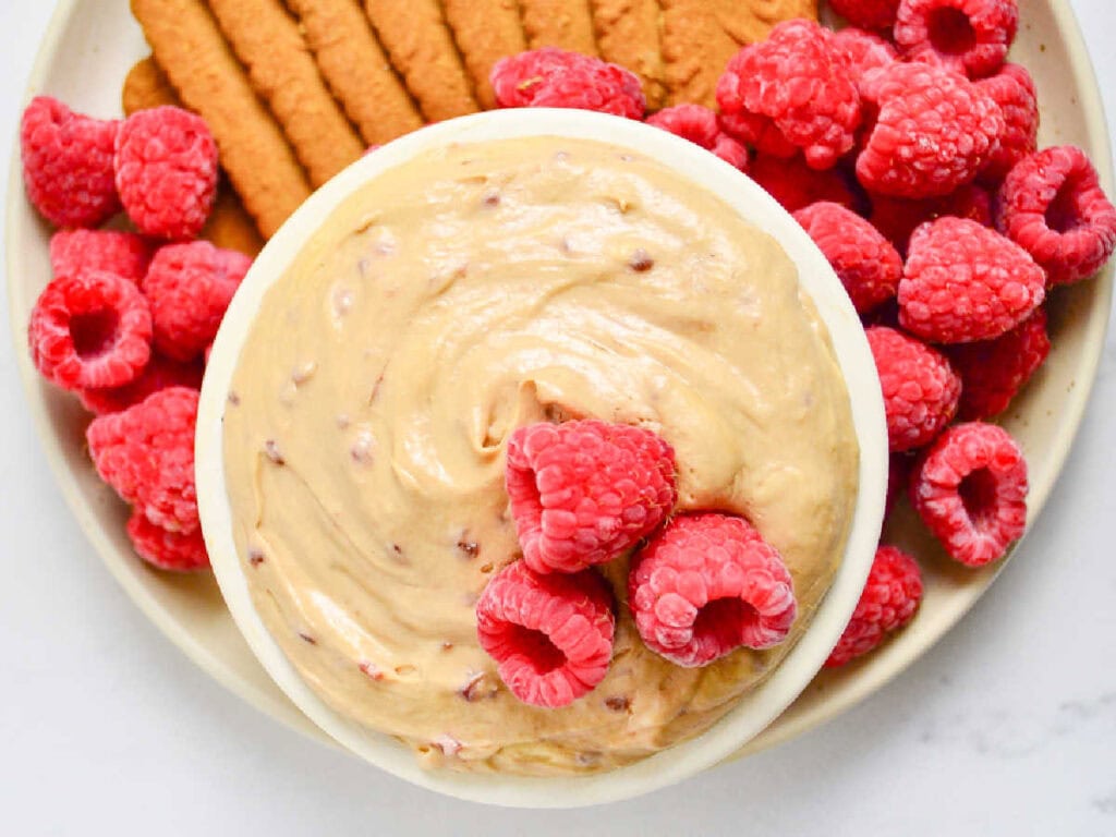 Top view of bowl of Biscoff cheesecake dip with whole raspberries and Lotus cookies.