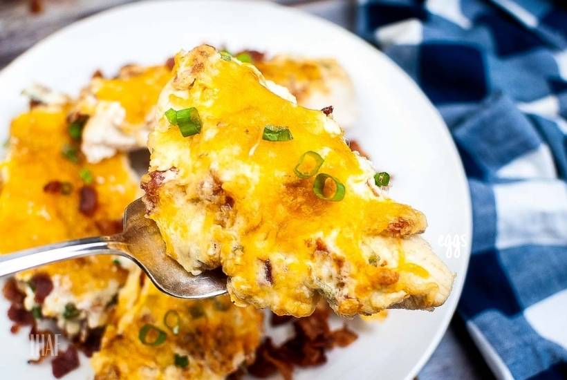 Closeup view of an air fried chicken breast topped with cheese, bacon and green onion on a fork.