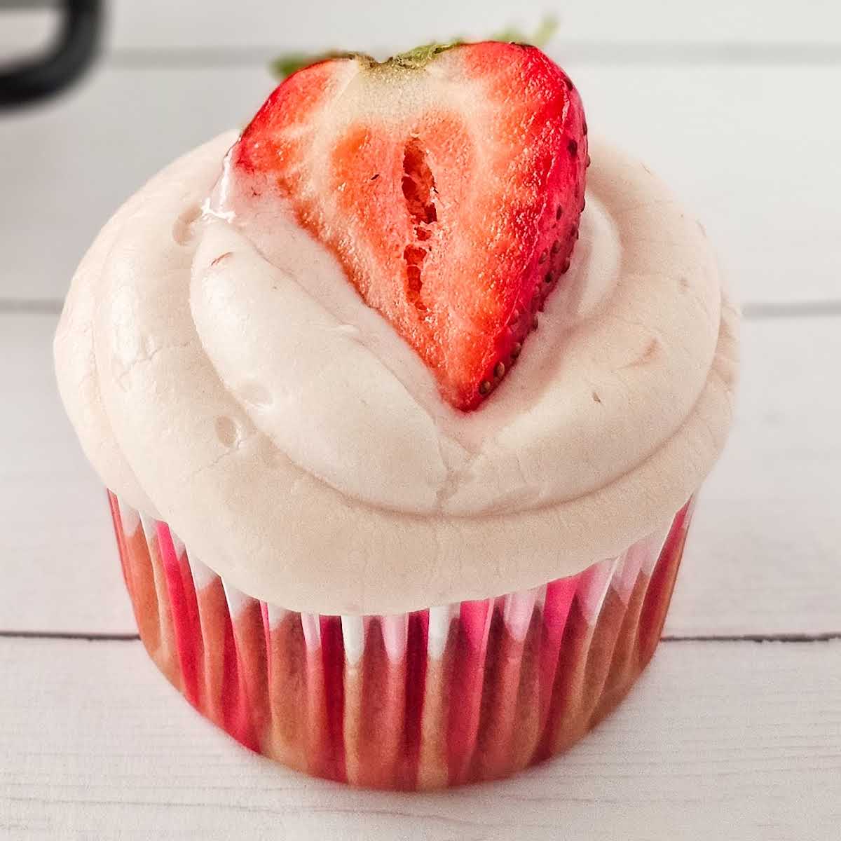 Closeup view of a strawberry cupcake with cream cheese frosting and garnished with a strawberry half.