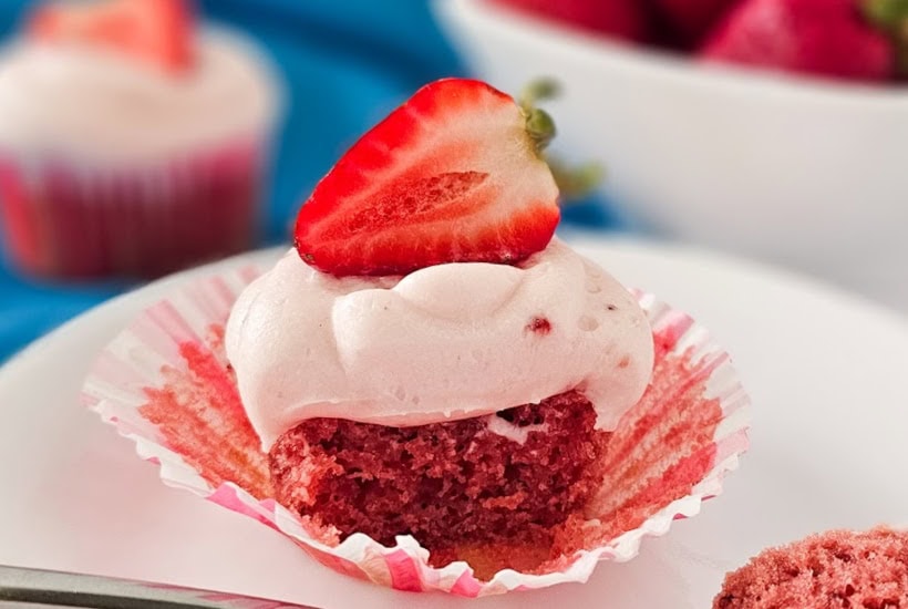 Half of a cupcake topped with cream cheese frosting and a strawberry half.