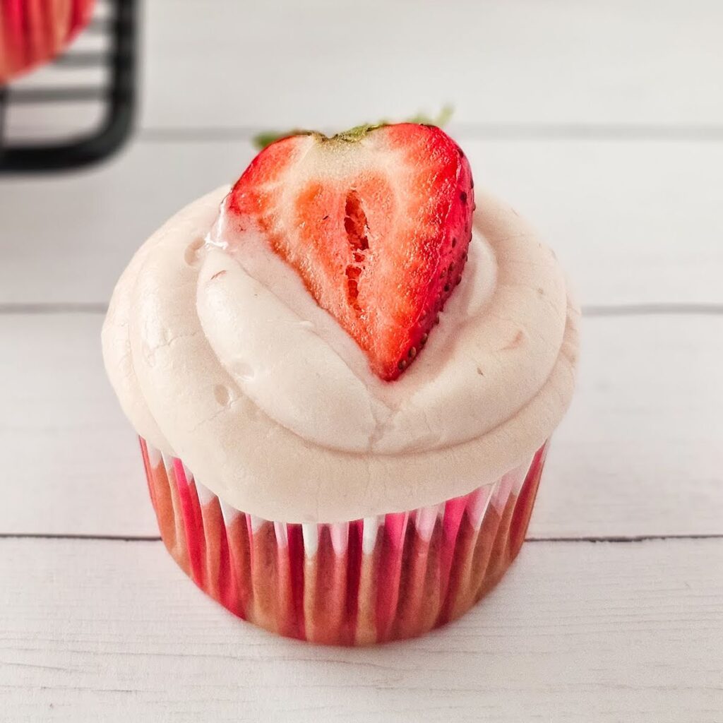 Closeup view of a frosted pink cupcake garnished with a strawberry half.